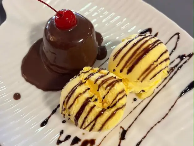 Pudim coberto de calda de chocolate com duas bolas de sorvete no prato