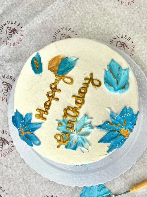 Bolo de aniversário com flores azuis pintadas à mão e escrita dourada