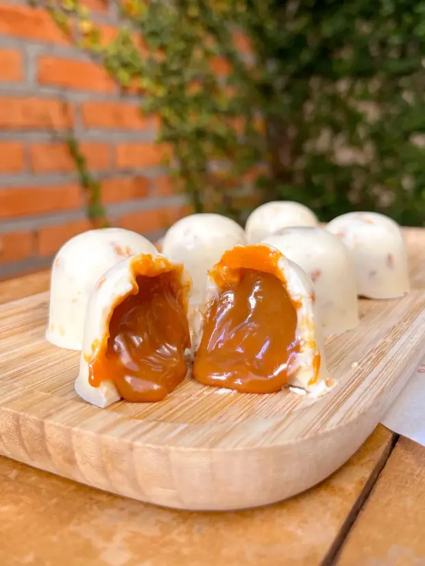 Bombons de chocolate branco recheados de doce de leite, um deles aberto