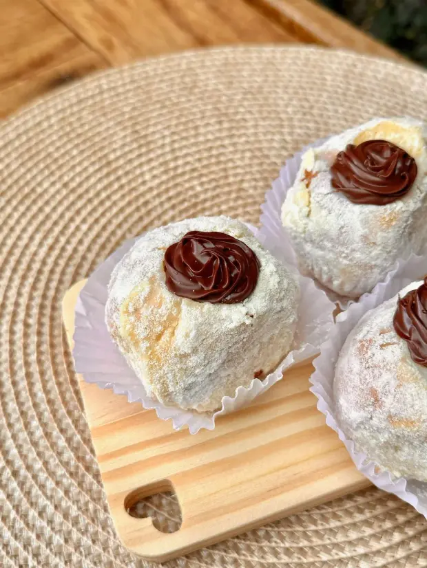 Sonhos polvilhados com açúcar e um bico de creme de avelã por cima, na tábua de madeira